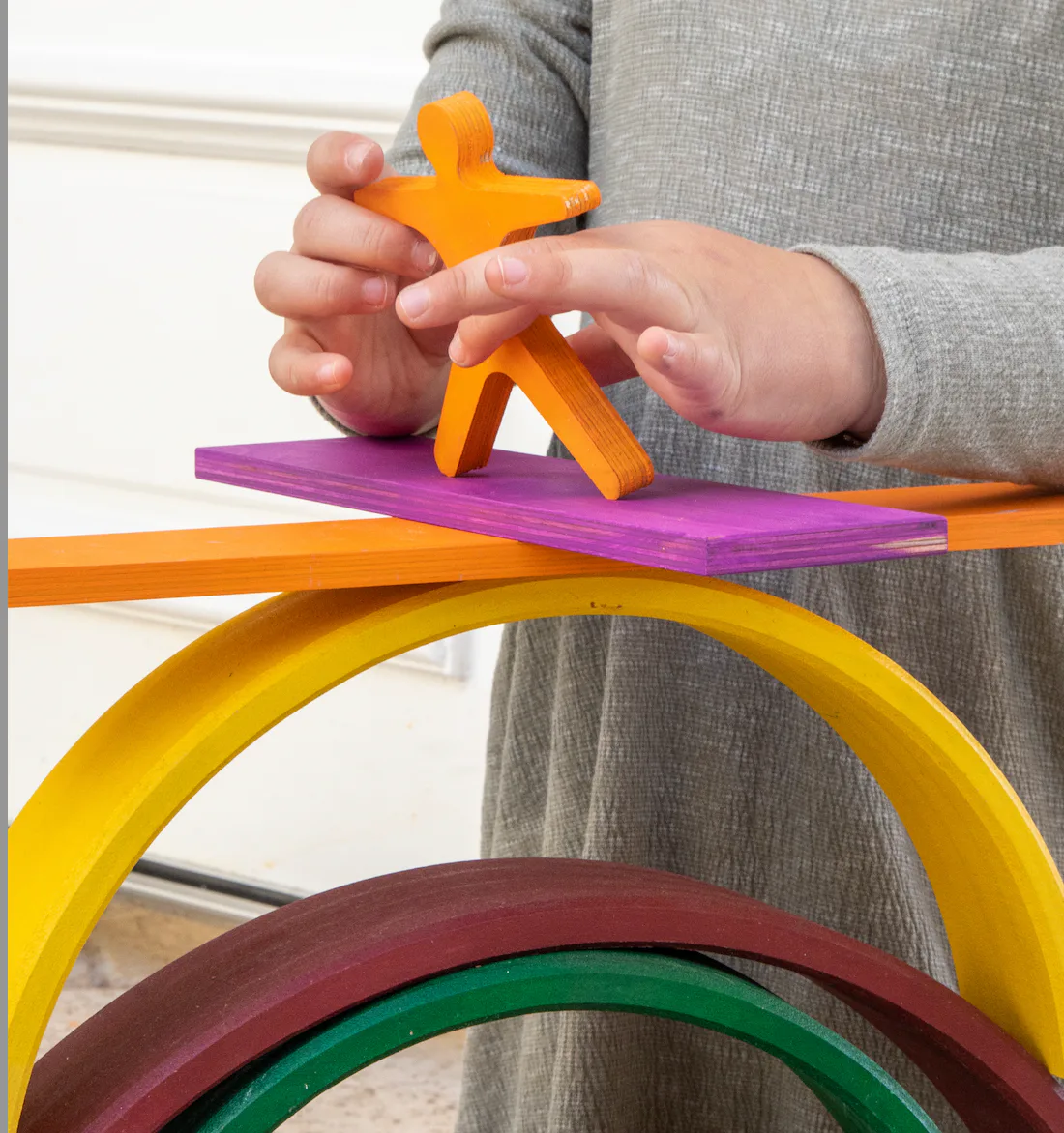 A child balancing a wooden figure on rainbow blocks