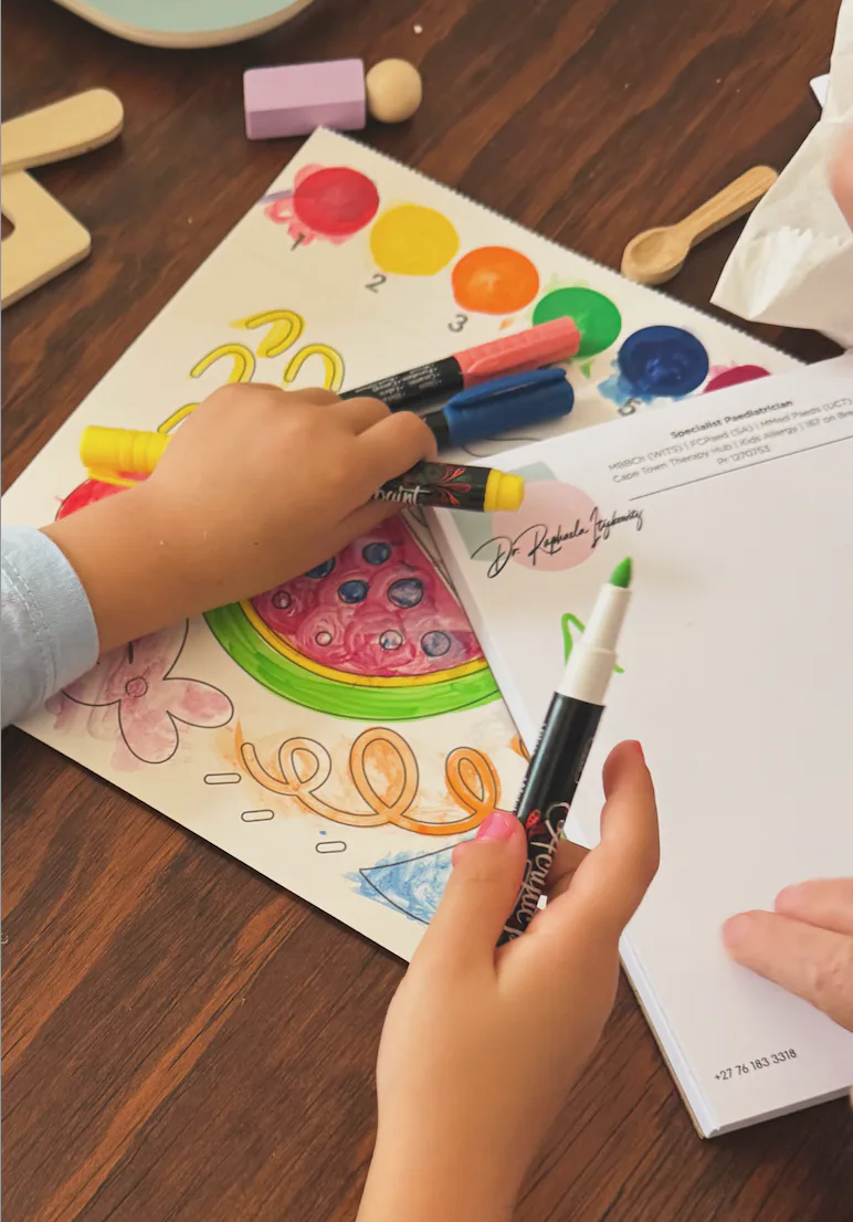 A child colouring in with paint pens beside Dr Itzikowitz's notepad