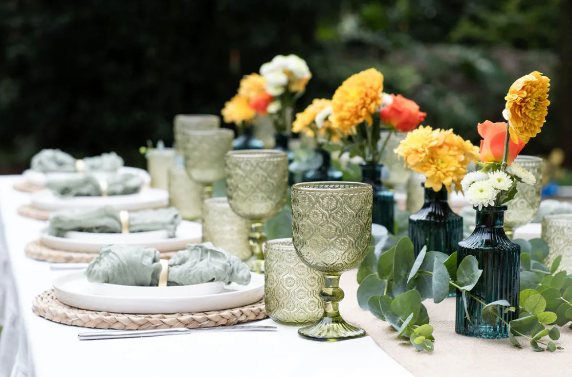 A coordinated outdoor tablescape with green glassware and yellow and orange flowers