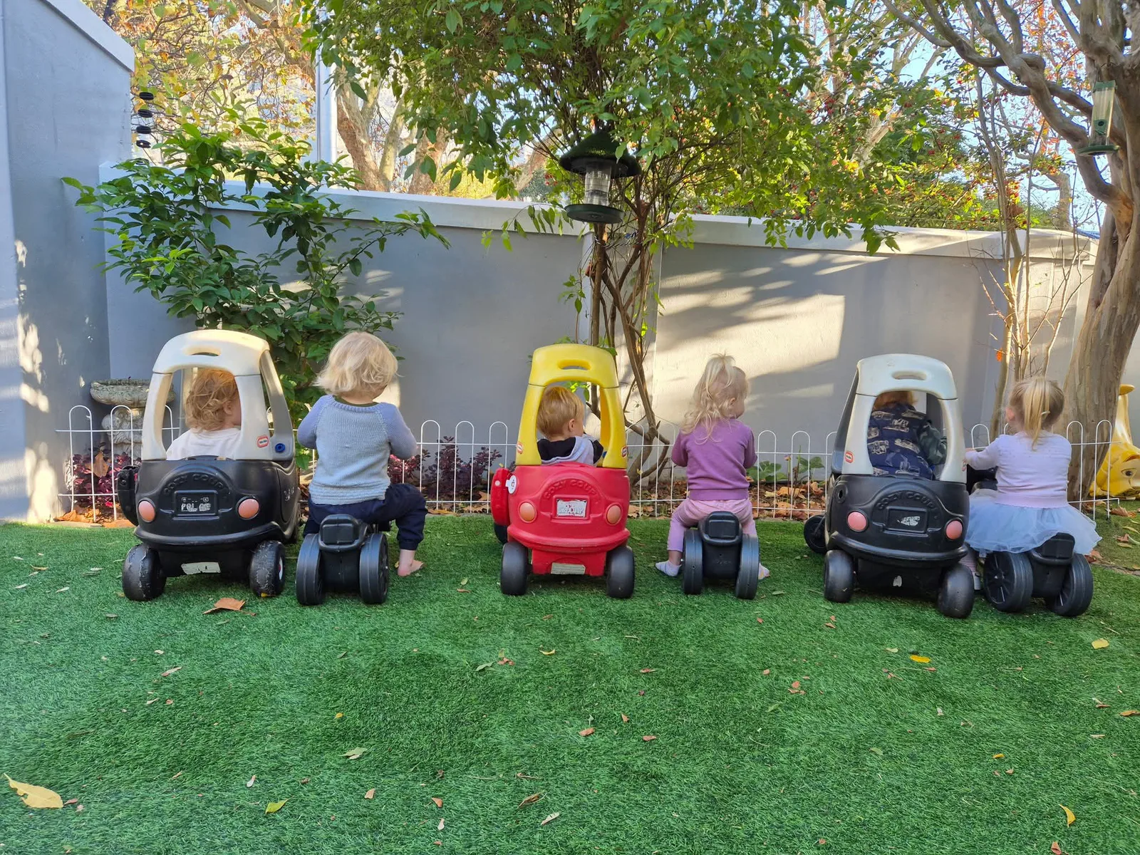 Children on ride-on cars along the garden fence at Lauren's Playschool