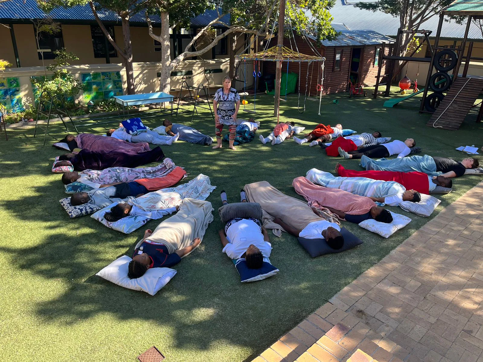 Teenagers lying in a circle on the grass with blankets and pillows during a breathwork session