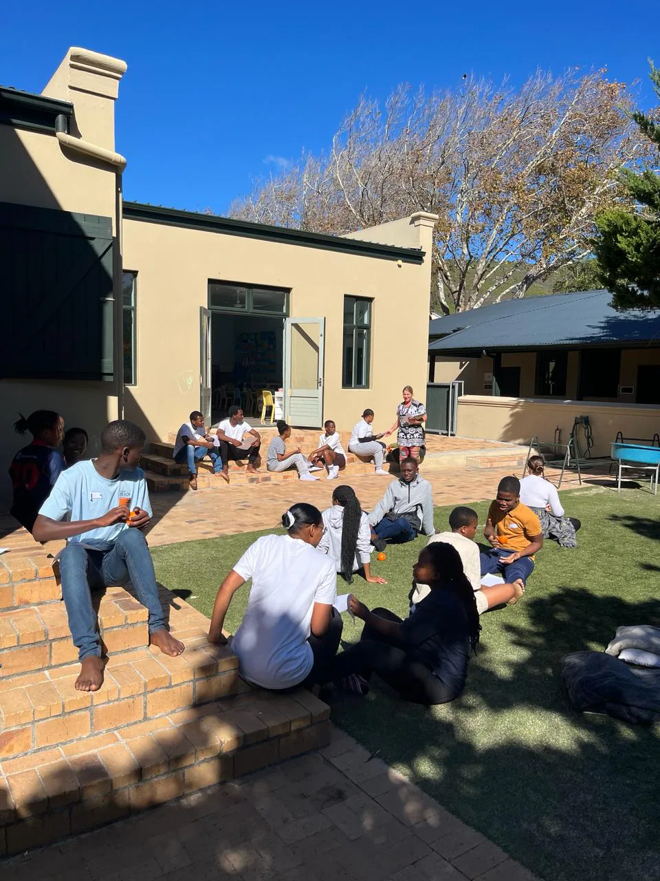 Teenagers sitting together on the steps and lawn between workshops