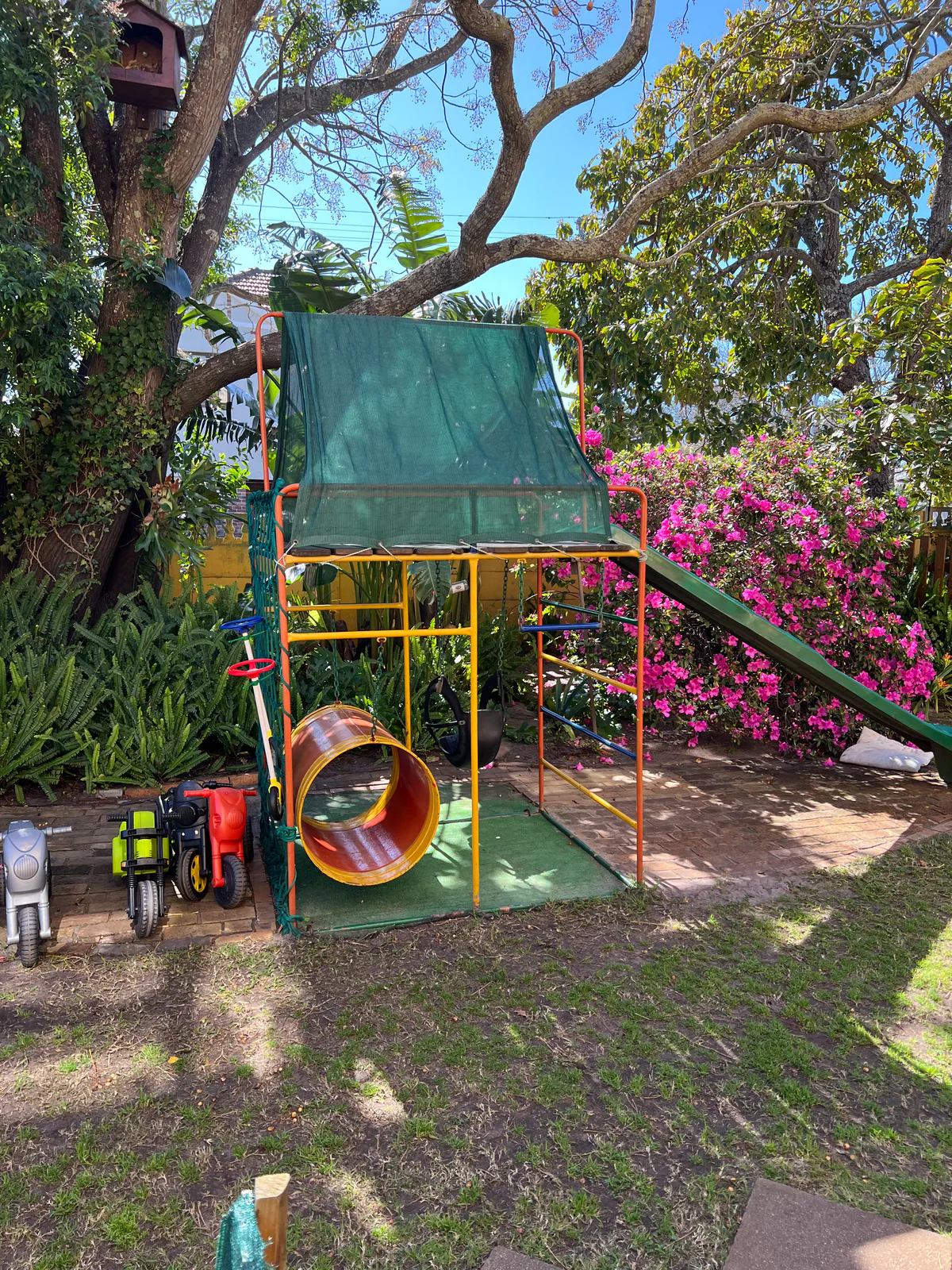 The garden, with a shaded jungle gym, slide, tunnel and swings under the trees