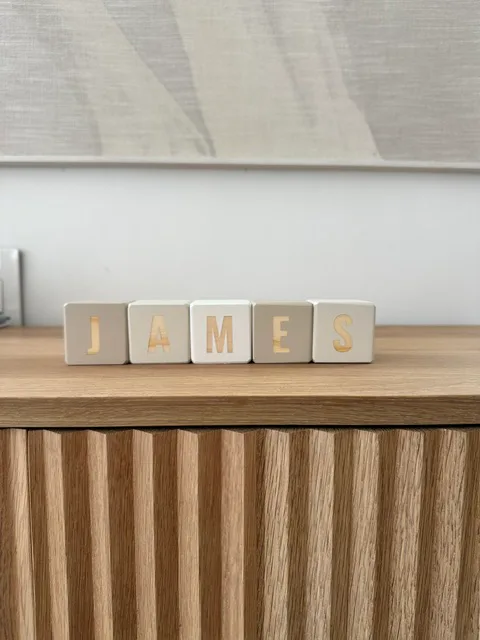 Blocks spelling James in a row on a fluted wooden sideboard
