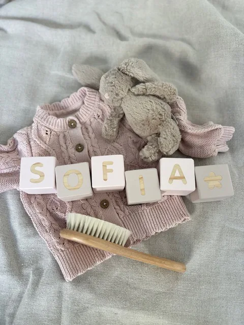 Blocks spelling Sofia laid out with a knitted cardigan, a bunny and a baby brush