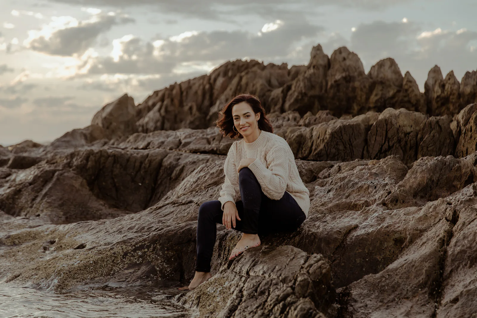 Nolene Adams seated on rocks beside the sea