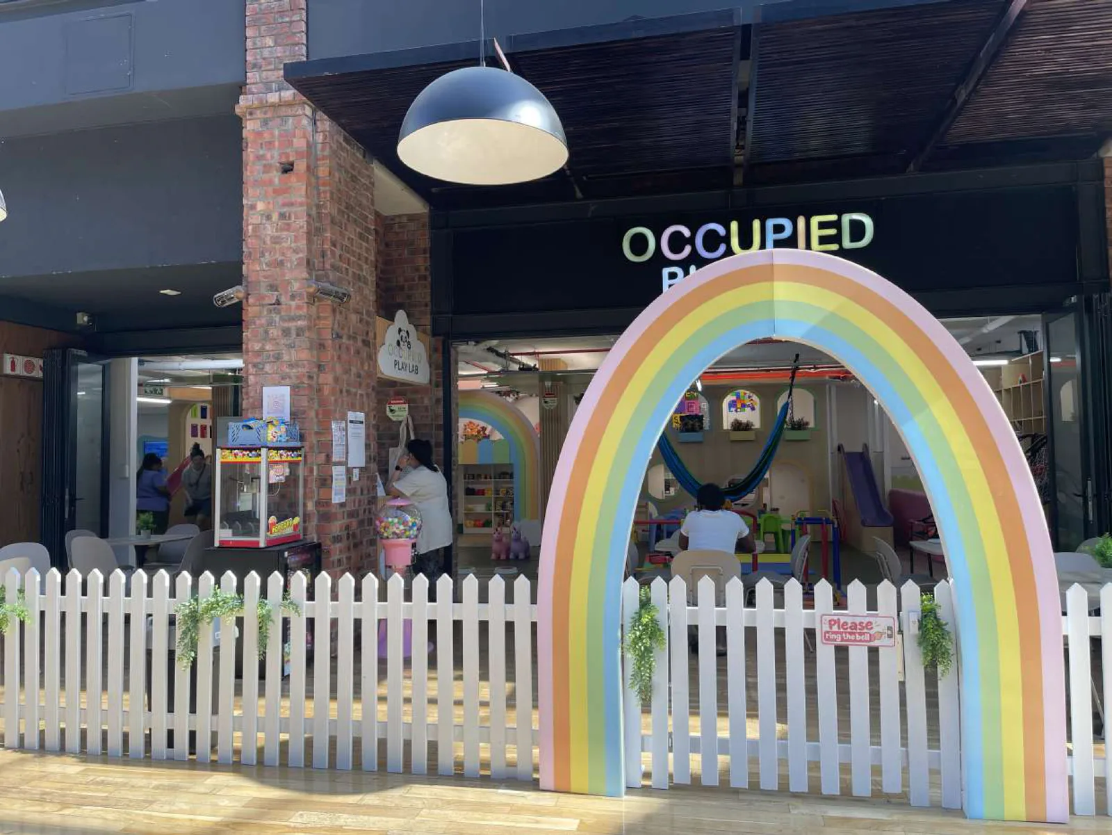 The Occupied Play Lab entrance at Wembley Square, with a rainbow arch and white picket fence
