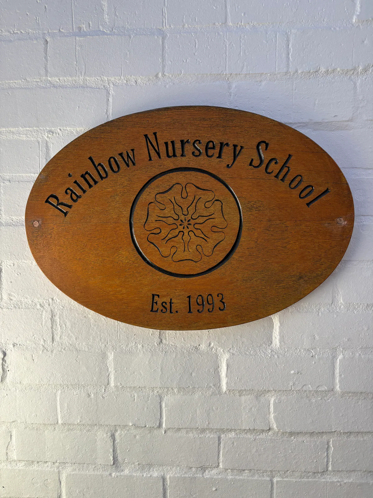 The carved wooden Rainbow Nursery School sign, marked Est. 1993, on a whitewashed brick wall