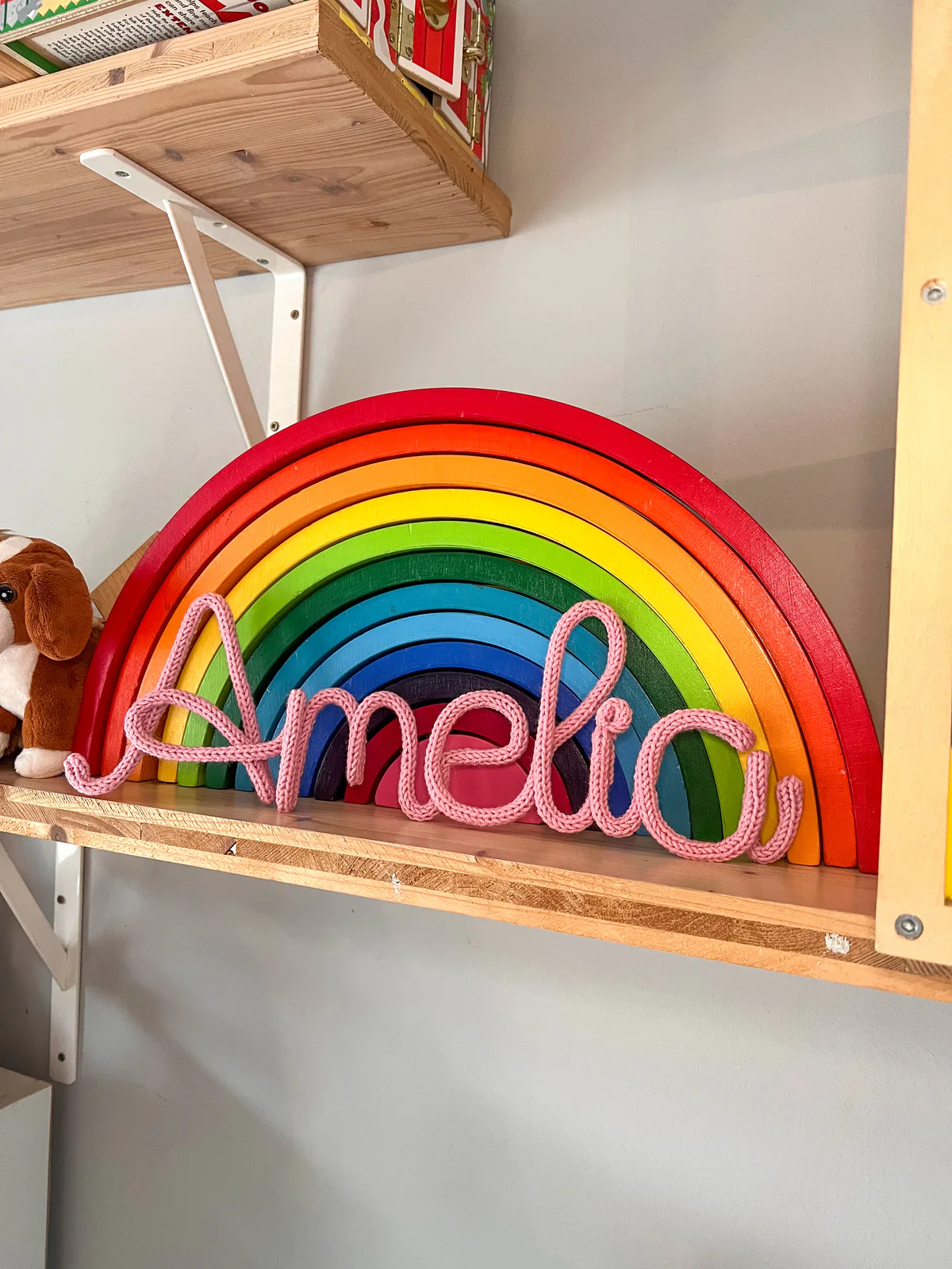 Pink knitted Amelia name sign displayed with a wooden rainbow